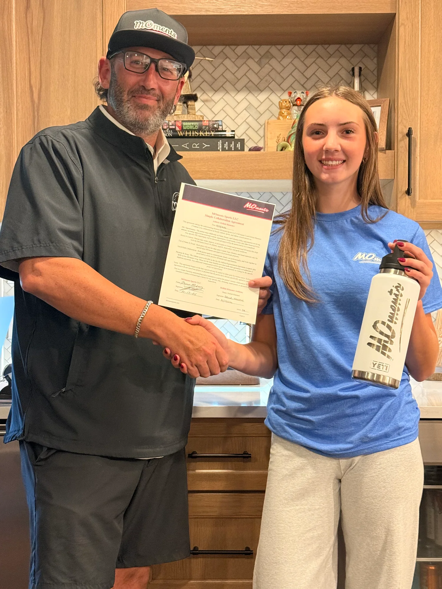 A MOments handshake with a signed agreement and white bottle